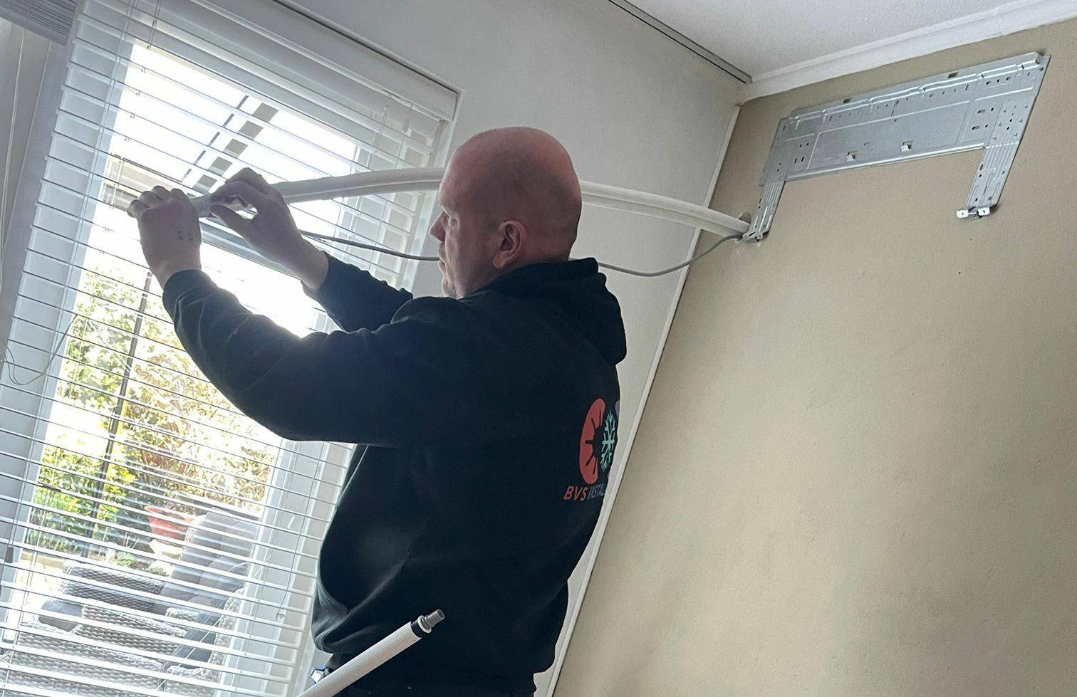 Afbeelding van een van de monteur van BVS-Installatie die een airco leiding monteert.